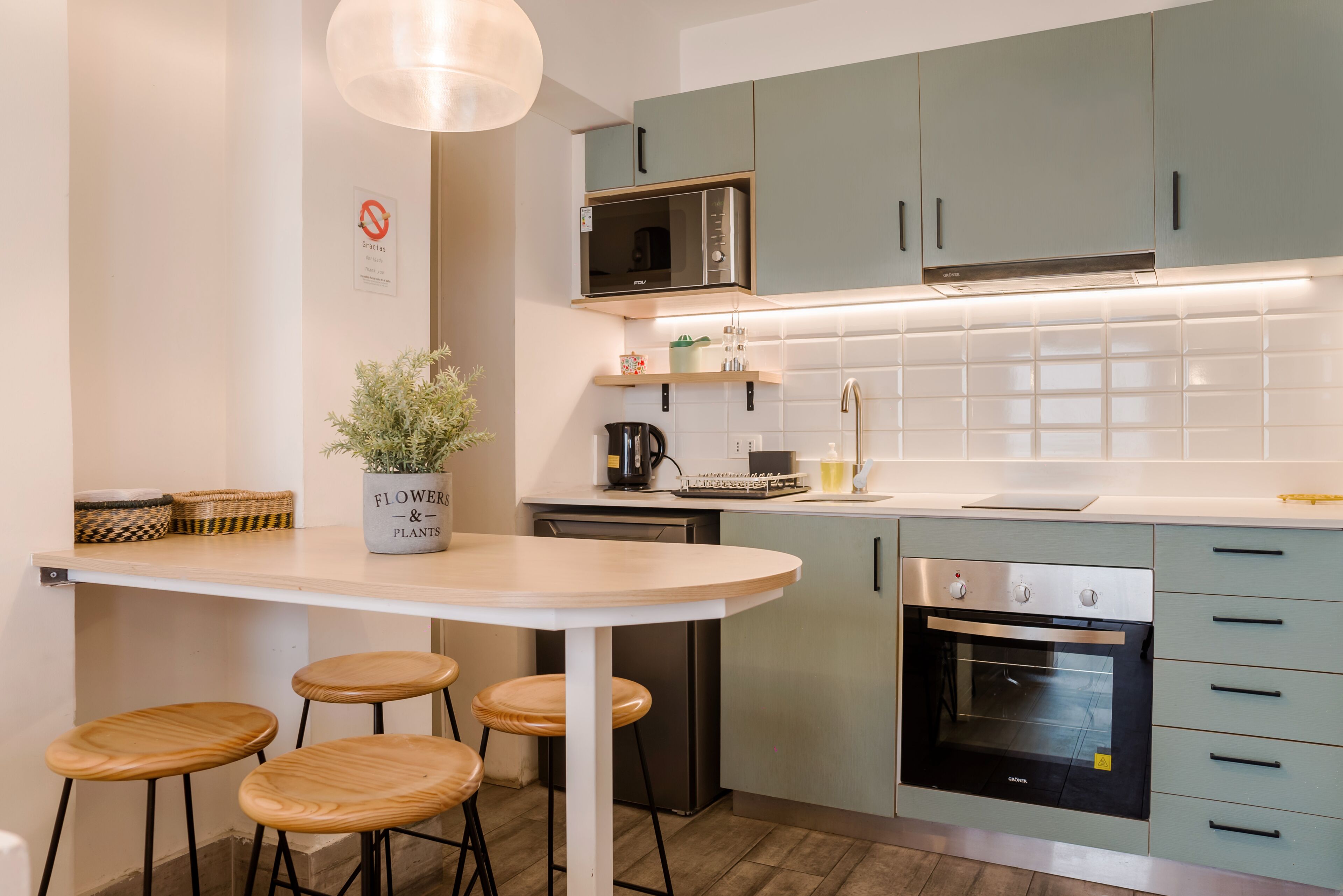 A modern kitchen with a round table, stools, a microwave, oven, and a potted plant.