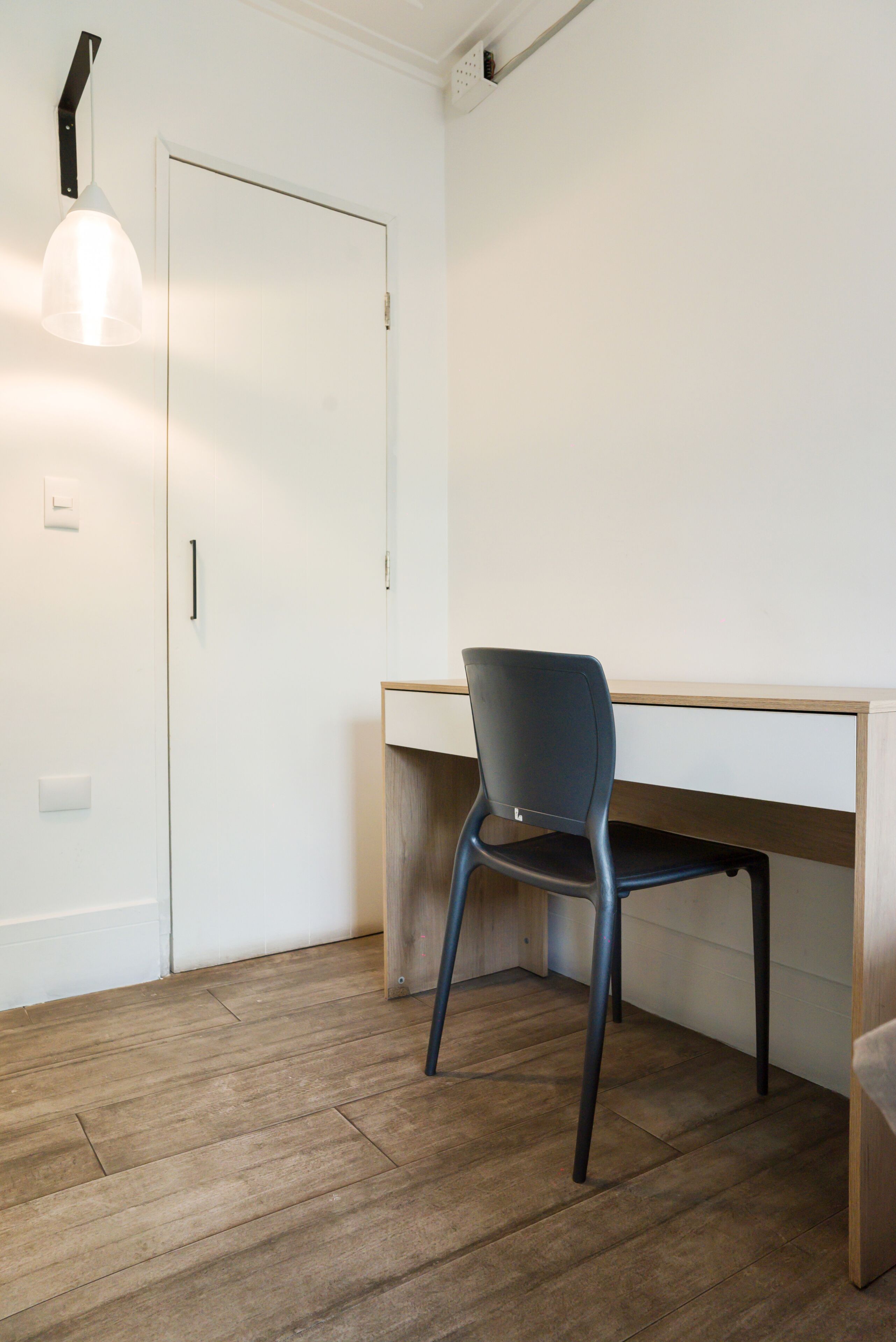 A room with a wooden desk, a chair, a door, and a pendant light.