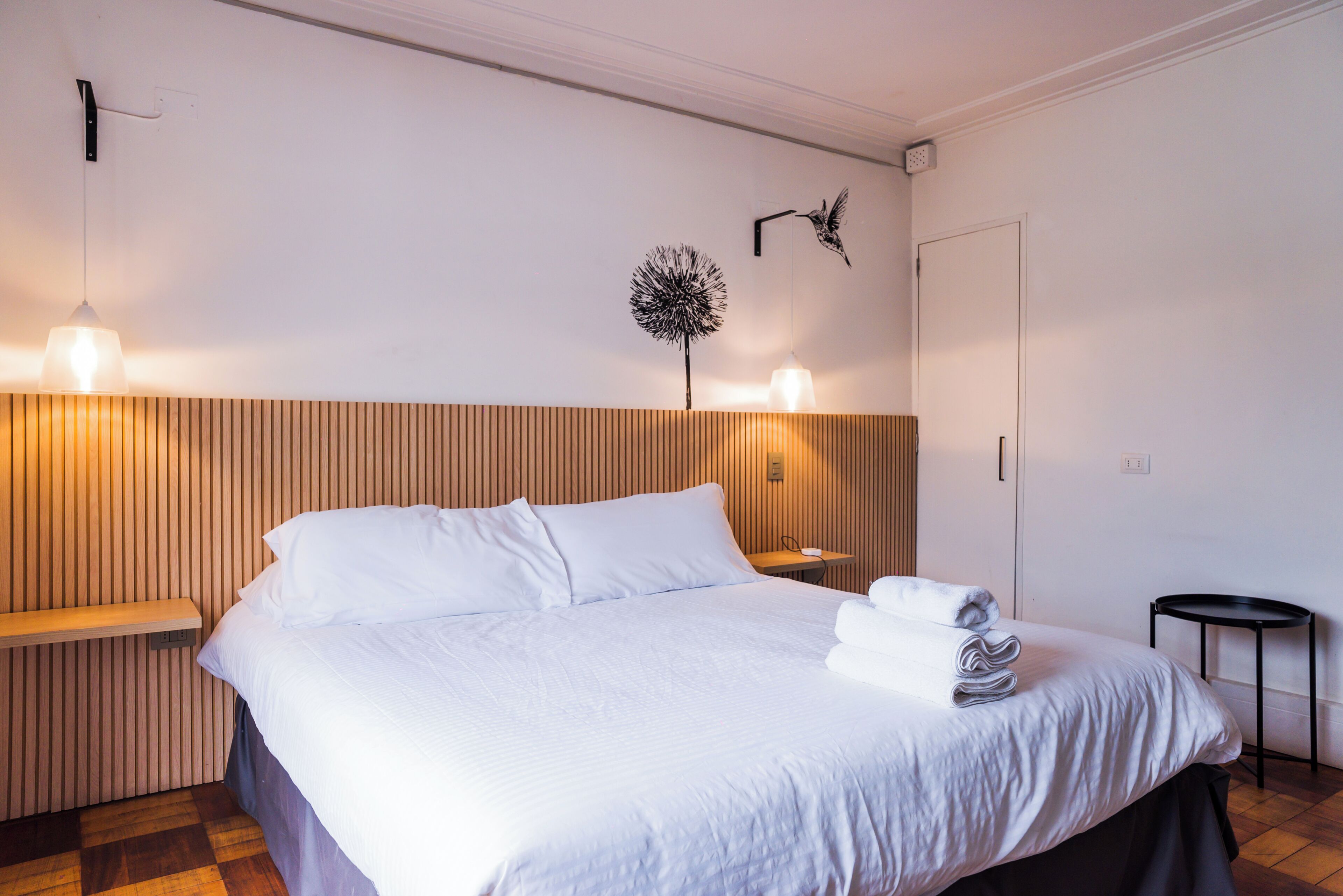 Habitación de hotel con cama, mesitas de noche, lámpara de pared y un adorno en la pared.
