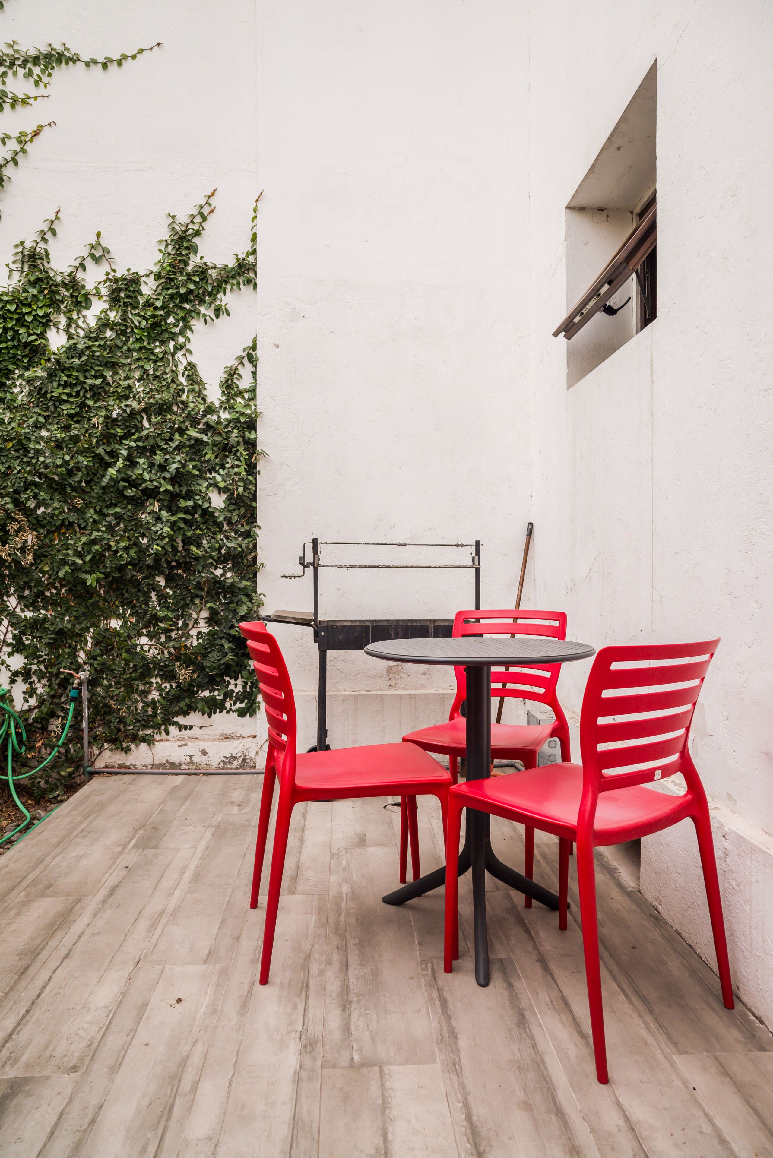 Eine Terrasse mit Tisch und roten Stühlen, ein Fenster und eine mit Efeu bewachsene Mauer.