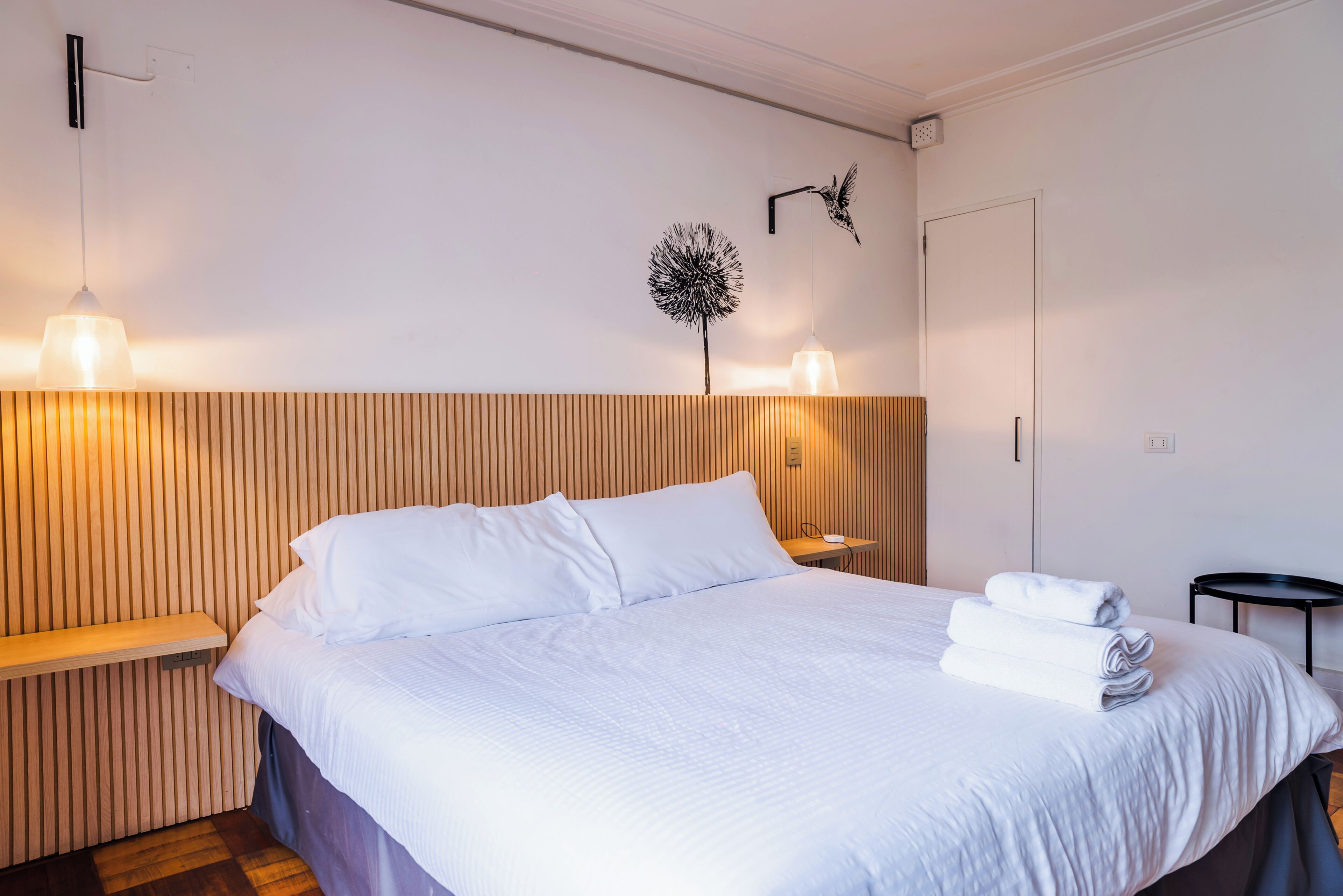 A neatly made bed with white linens, a wooden headboard, and two wall-mounted lamps.