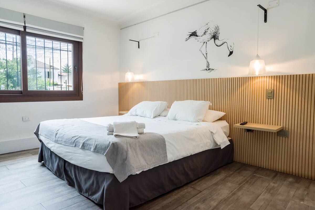 Quarto com cama, janela, prateleira na parede e arte na parede com um pássaro.