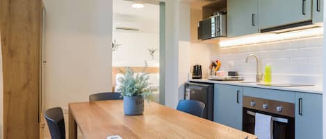 A compact kitchen with a wooden table, chairs, a microwave, and a dishwasher.