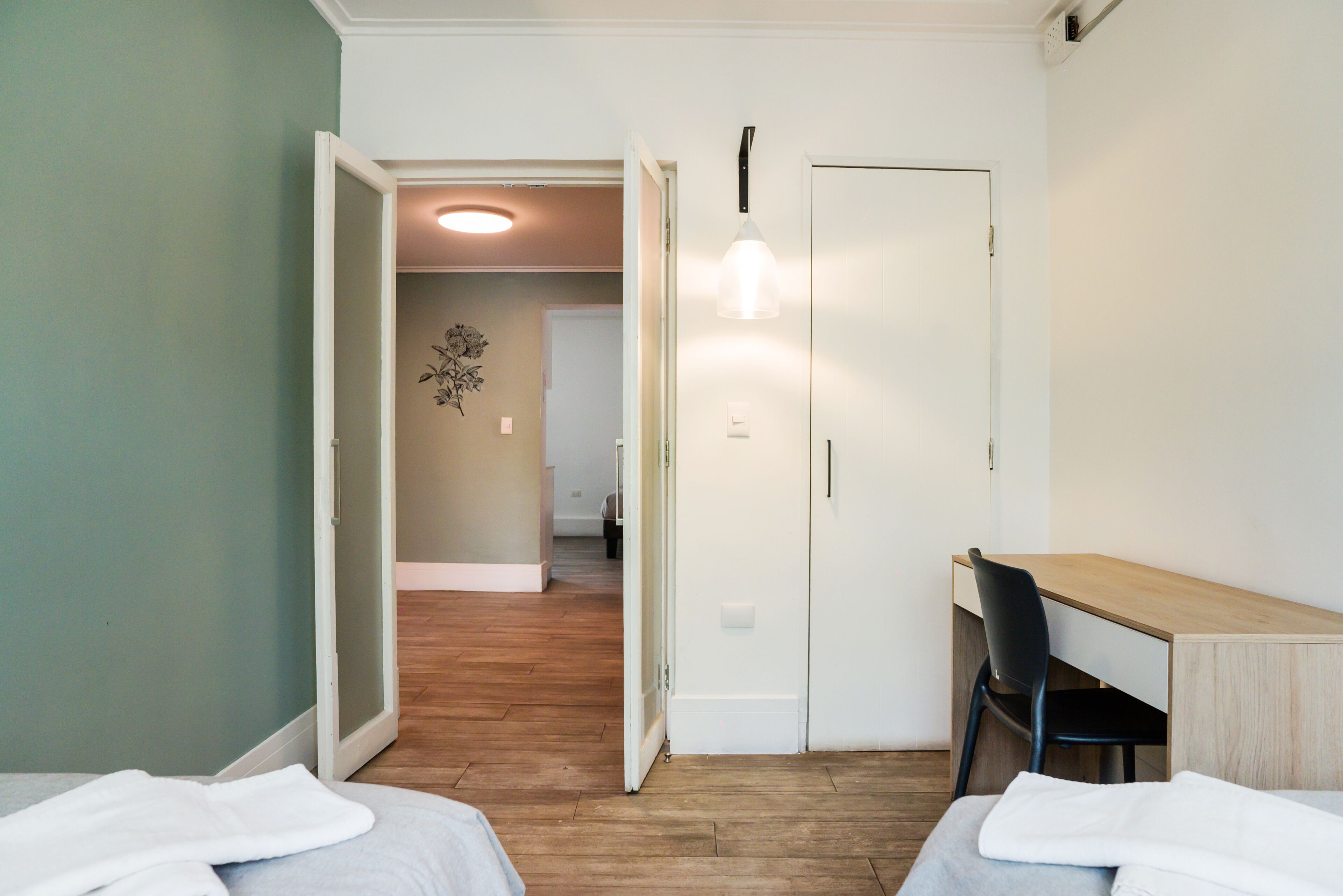 Een kamer met een bed, een bureau en een stoel. Er is een deur die naar een andere kamer leidt.