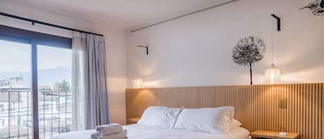 A hotel room with a bed, a nightstand, a wall-mounted lamp, and a view of the outside.