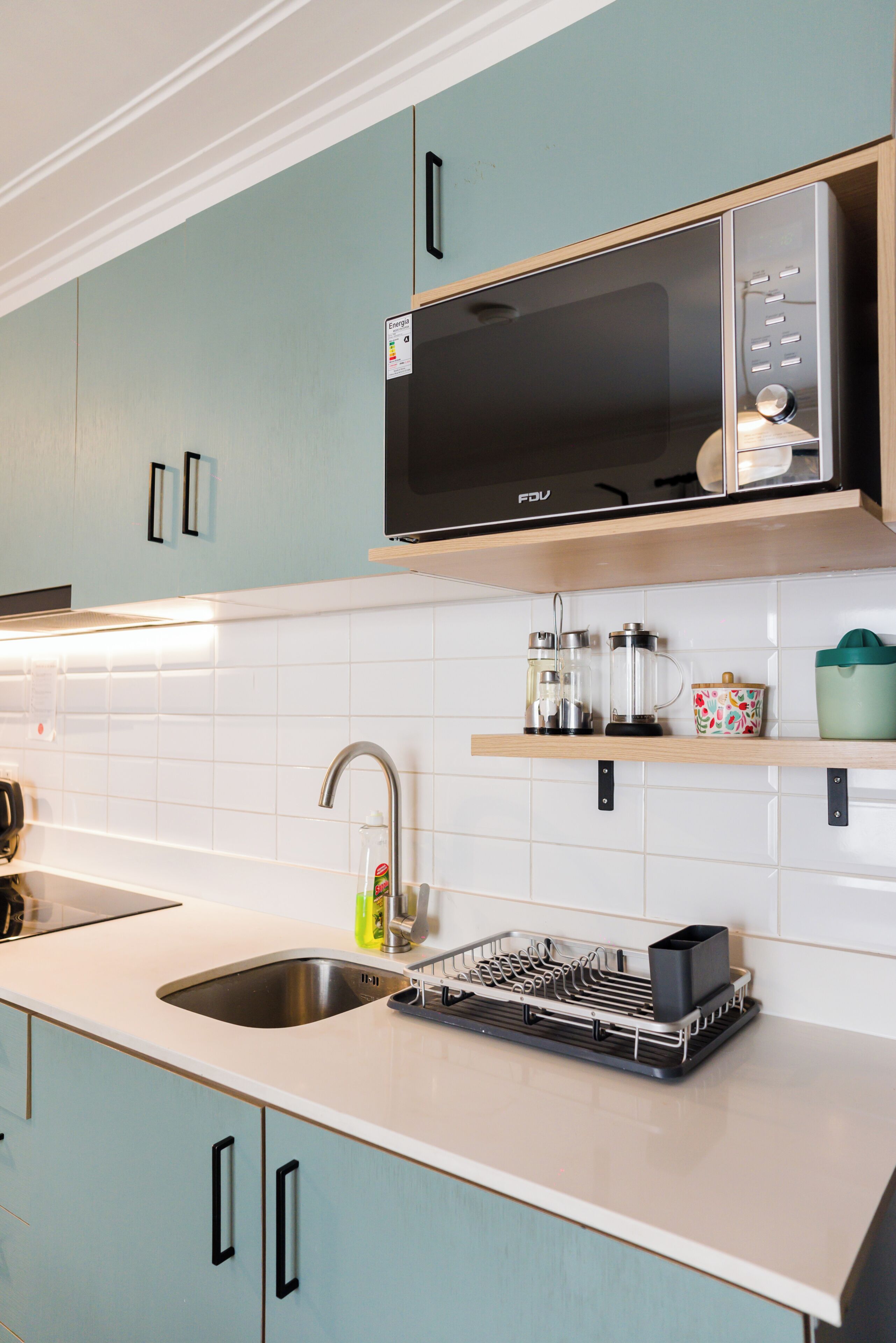 A kitchen with a microwave, sink, and dish drying rack.