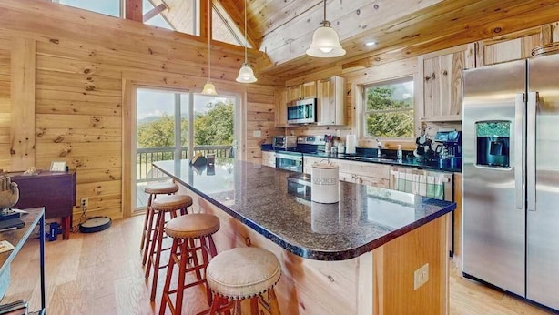 Een moderne keuken met houten wanden, een centraal kookeiland met krukken, roestvrijstalen apparatuur en grote ramen.