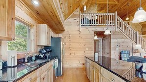 Een houten hut binnen met een keuken, een trap en een balkon.