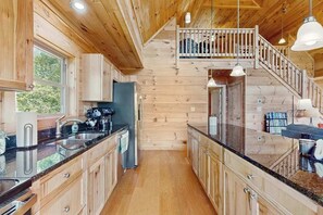 Ein Holzblockhaus-Interieur mit Küche, einer Treppe und einem Balkon.