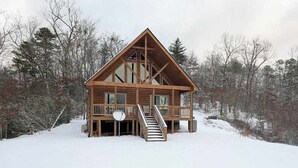 Een houten chalet met balkon, trap en uitzicht op het omliggende bos.