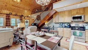Un interior de cabaña acogedor con comedor, cocina y una escalera que lleva a un nivel superior.