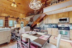 A wooden interior with a dining table, chairs, a chandelier, a staircase, and kitchen cabinets.