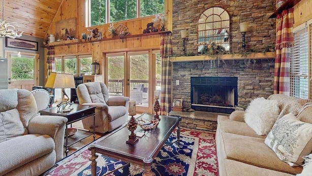 Una sala de estar acogedora con chimenea de piedra, ventanas amplias y techo de madera.