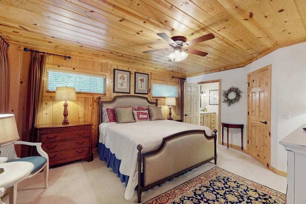 Une chambre à coucher avec un plafond en bois, un lit, une table de chevet, une chaise, une commode et une fenêtre avec des rideaux.