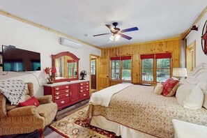 Une chambre à coucher comprenant un lit, une commode, un téléviseur, un ventilateur de plafond et de grandes fenêtres.