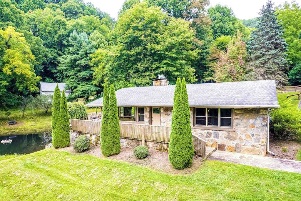 Une maison en pierre avec un étang, entourée d’une végétation luxuriante.