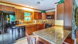 A kitchen with granite countertops, wooden cabinets, a refrigerator, a dishwasher, and a microwave. - The Rock House at Big Bear Estates (Waynesville)