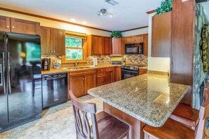 Una cocina con encimeras de granito, armarios de madera, un refrigerador, un lavavajillas y un microondas.