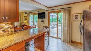 A kitchen with a granite countertop, wooden cabinets, a built-in dishwasher, and a large window leading to an outdoor patio. - The Rock House at Big Bear Estates (Waynesville)
