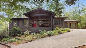 Een houten vakantiehuis met twee verdiepingen en een veranda, omgeven door groen.