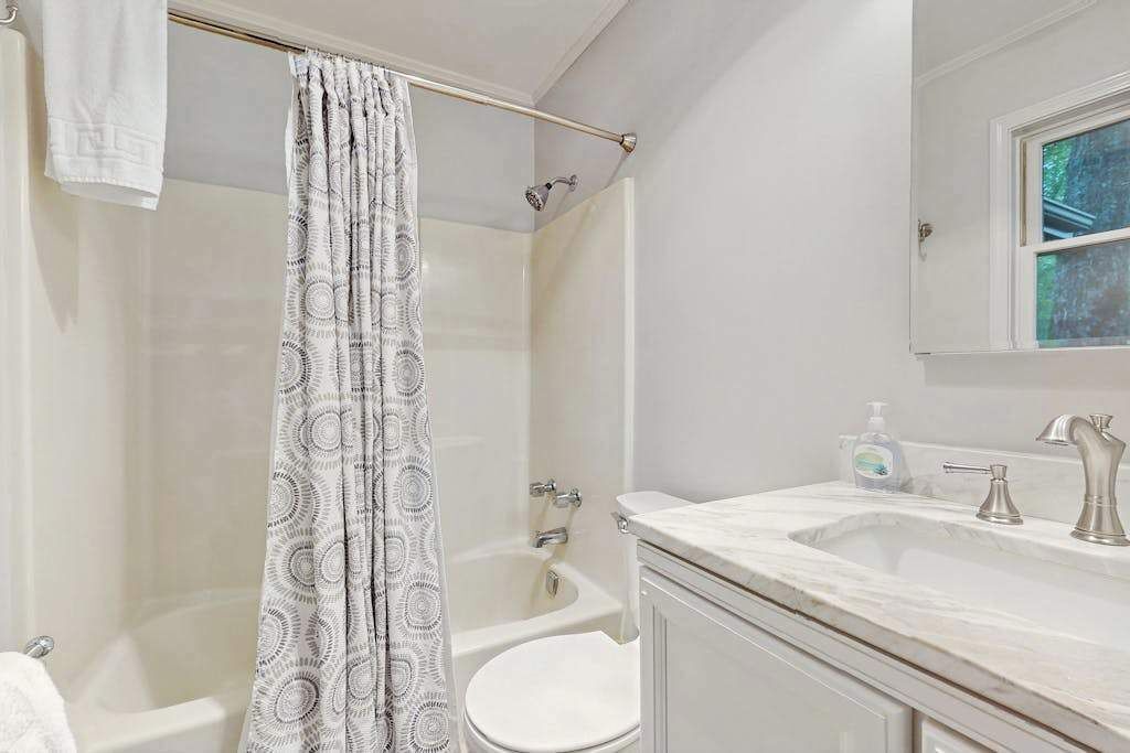 Un baño con cortina de ducha, bañera, inodoro, lavabo y espejo.