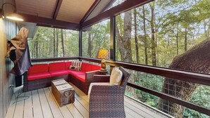 Een overdekt terras met een rode bank, rieten stoelen en een lamp.