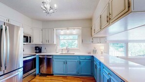 Una cocina con armarios blancos, encimera azul, refrigerador de acero inoxidable, microondas y lavavajillas.