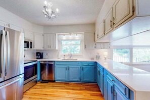 A kitchen with white cabinets, a blue countertop, a stainless steel refrigerator, a microwave, and a dishwasher. - Blue Ridge Cottage (Waynesville)