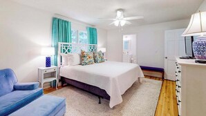 Un dormitorio con cama, mesita de noche, silla, escritorio y ventilador de techo.
