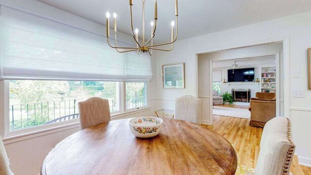 Un comedor con mesa de madera, sillas, una araña y vistas amplias a través de grandes ventanales.