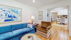 Una sala de estar con un sofá azul, un sillón marrón, una mesa de centro redonda y un cuadro en la pared.