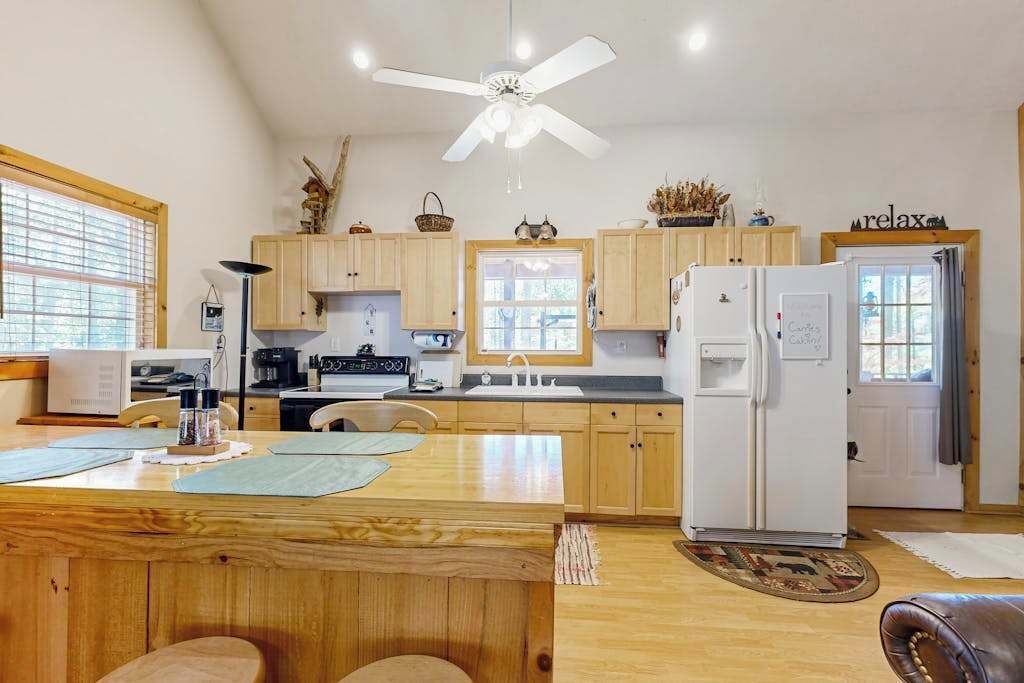 A kitchen with wooden cabinets, a white refrigerator, a ceiling fan, and a dining area with a wooden table and chairs.