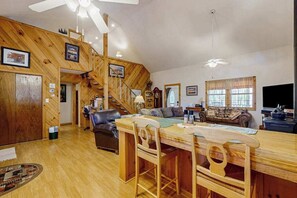 A spacious living area with a wooden staircase, a dining table with chairs, a sofa, and a television. - Carrie’s Cabin (Sylva)