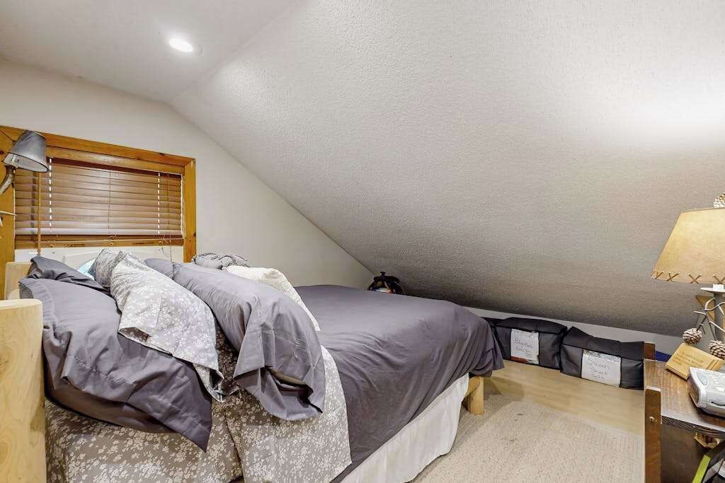 A small, cozy room with a bed, a nightstand, a lamp, and a window with blinds.