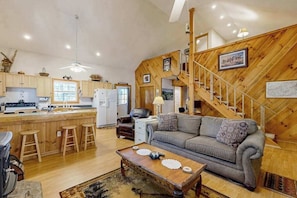 A spacious living area with a wooden staircase, a kitchen with wooden cabinets, and a bar area. - Carrie’s Cabin (Sylva)