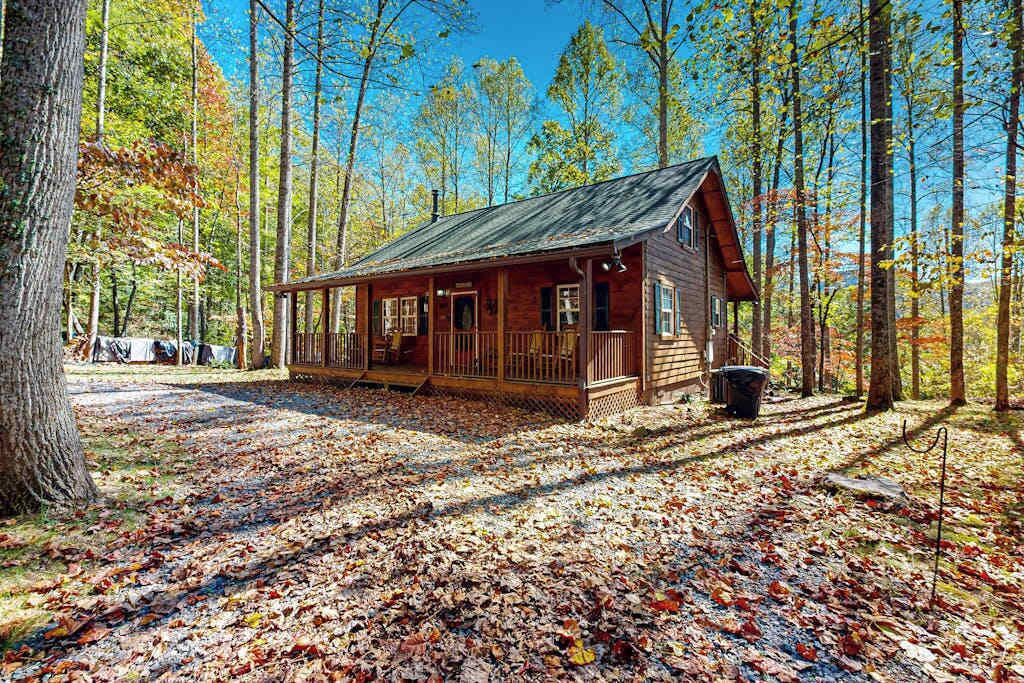 A rustic cabin with a porch, surrounded by a forest with autumn leaves.