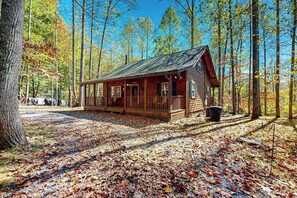 A rustic cabin with a porch, surrounded by a forest with autumn leaves. - Carrie’s Cabin (Sylva)