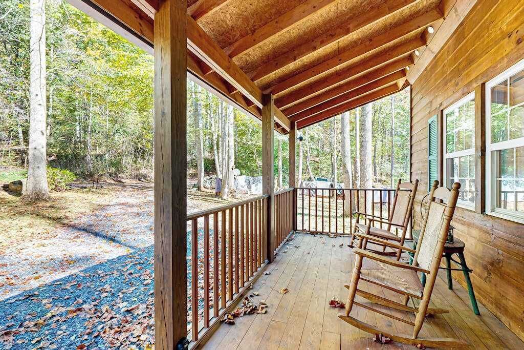 A wooden porch with a railing, rocking chairs, and a view of a forested area.