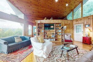 A cozy living room with a wooden ceiling, a television, a bookshelf, and a red cabinet.