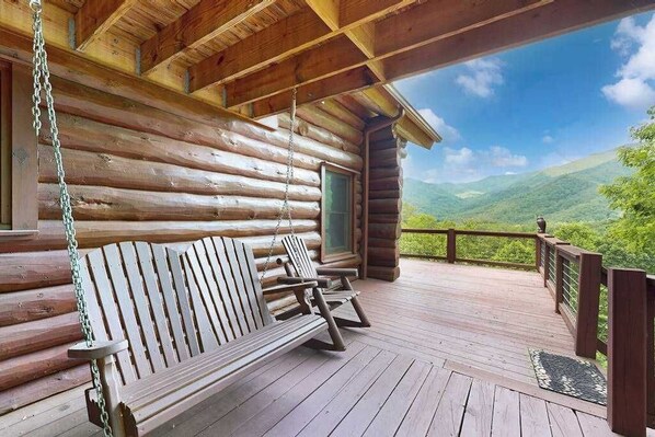 Eine Holzhütte mit Veranda, einer Schaukel und Blick auf grüne Hügel.