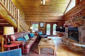 Ein rustikales Blockhaus-Interieur mit Ledersofa, Kamin aus Naturstein und Holzbalkendecke.
