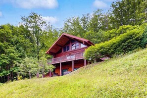 Eine Hütte mit Balkon, umgeben von viel Grün und Bäumen.