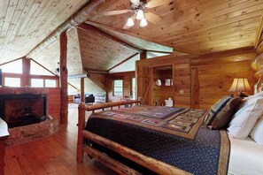 Ein Innenraum einer Blockhütte mit einem Bett, einem Kamin, einer Holzbalkendecke und einem Deckenventilator.