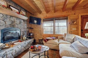 A cozy cabin interior with a stone fireplace, wooden walls, a television, a sofa, and a window. - Bear Hug (Sylva)