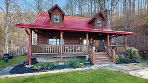 A log cabin with a porch, a chimney, and a stone foundation. - Bear Hug (Sylva)