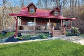 A log cabin with a porch, a chimney, and a stone foundation. - Bear Hug (Sylva)