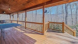 Um deck de madeira com mesa de pingue-pongue, guarda-corpos e vista para uma área montanhosa arborizada.