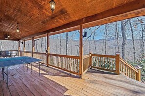 A wooden deck with a ping pong table, railings, and a view of a forested mountain area. - Timberwolf (Tuckasegee)