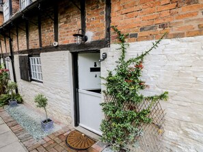 Um edifício tradicional em estilo de enxaimel, com uma porta branca, um pequeno jardim com plantas em vasos e um portão de metal.