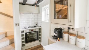 A compact kitchen with white cabinets, a built-in oven, a coffee machine, and storage jars labeled tea, coffee, and sugar. - 4 Masons Court (Stratford-upon-Avon)